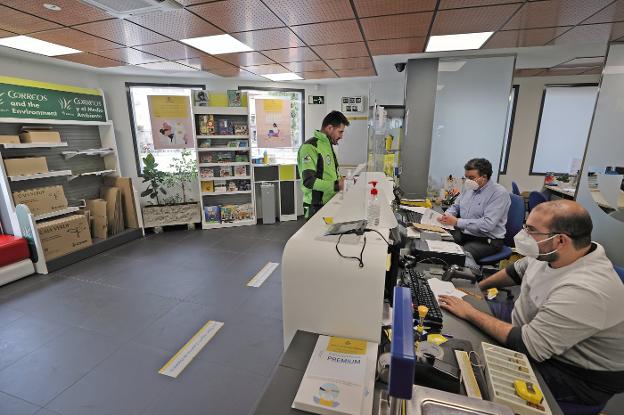 Trabajadores con mascarilla y un usuario, sin ella, ayer, en la oficina de Correos de Cabezón. 