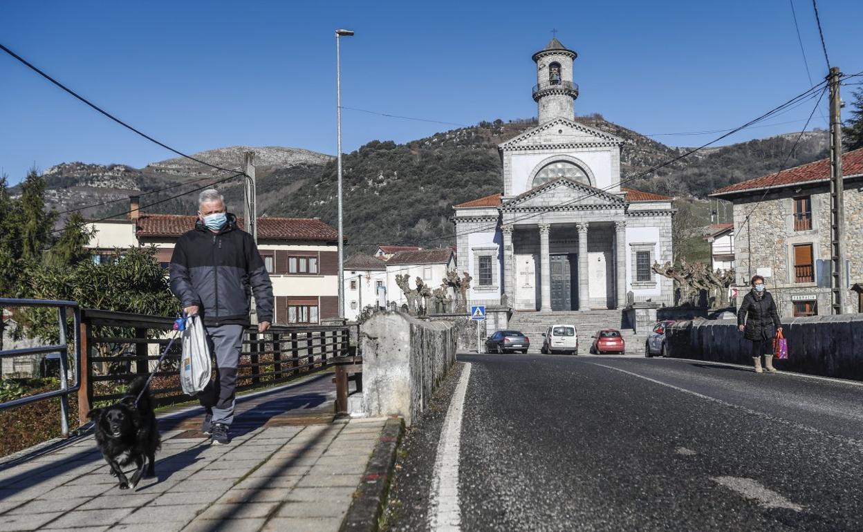 Un vecino camina con su perro por el puente de Arredondo, con la iglesia y su conocida torre al fondo.