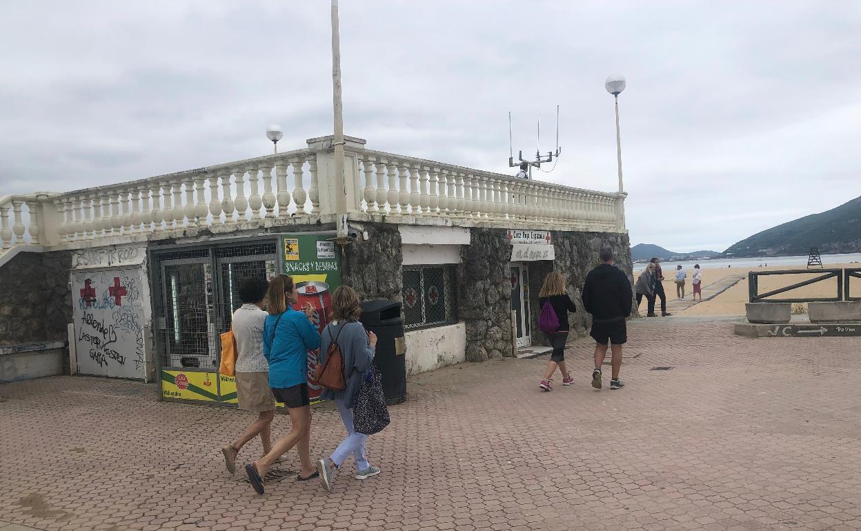 Paseantes transitan junto a la base de salvamento y socorrismo situada en la entrada principal a la playa Salvé de Laredo 