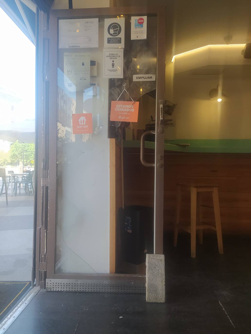 Puerta destrozada en el restaurante El Diocesano (calle Cádiz) y el bloque que usaron para romper el cristal.