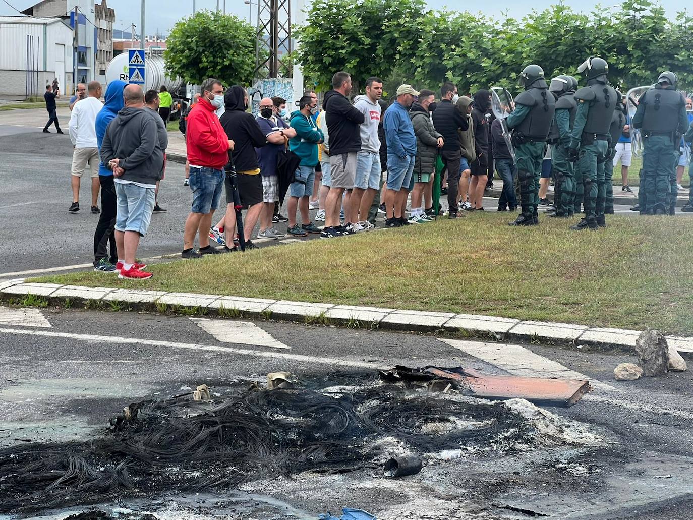 Restos de los neumáticos quemados en Guarnizo en primer plano y trabajadores y Policía al fondo.