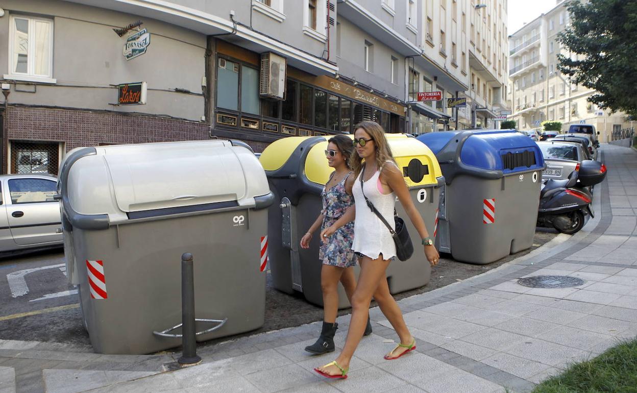 Dos jóvenes pasean ante unos contenedores urbanos en la capital cántabra.