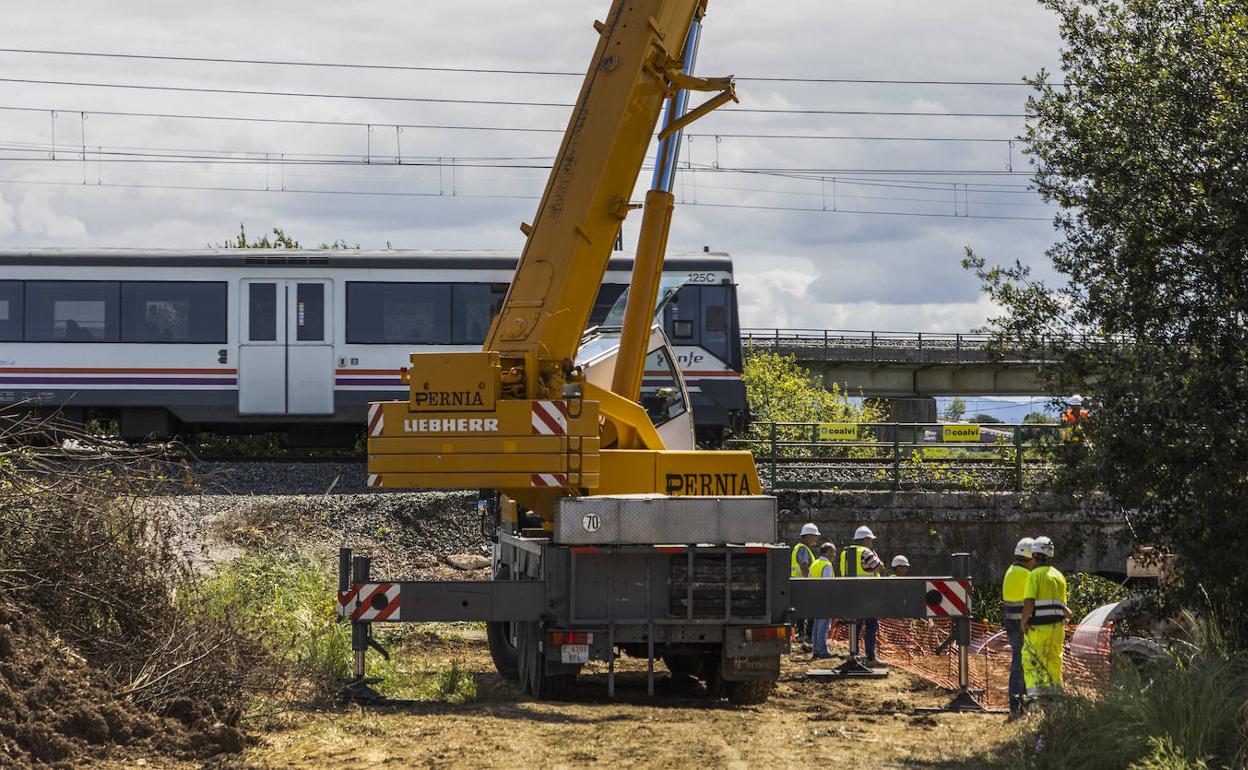 Varios operarios trabajan en el Canal de Raos al paso de un tren de Cercanías