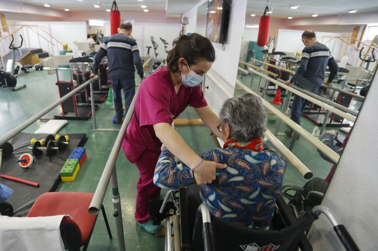 Una terapeuta ayuda a una mujer a incorporarse en el centro hospitalario Padre Menni. 