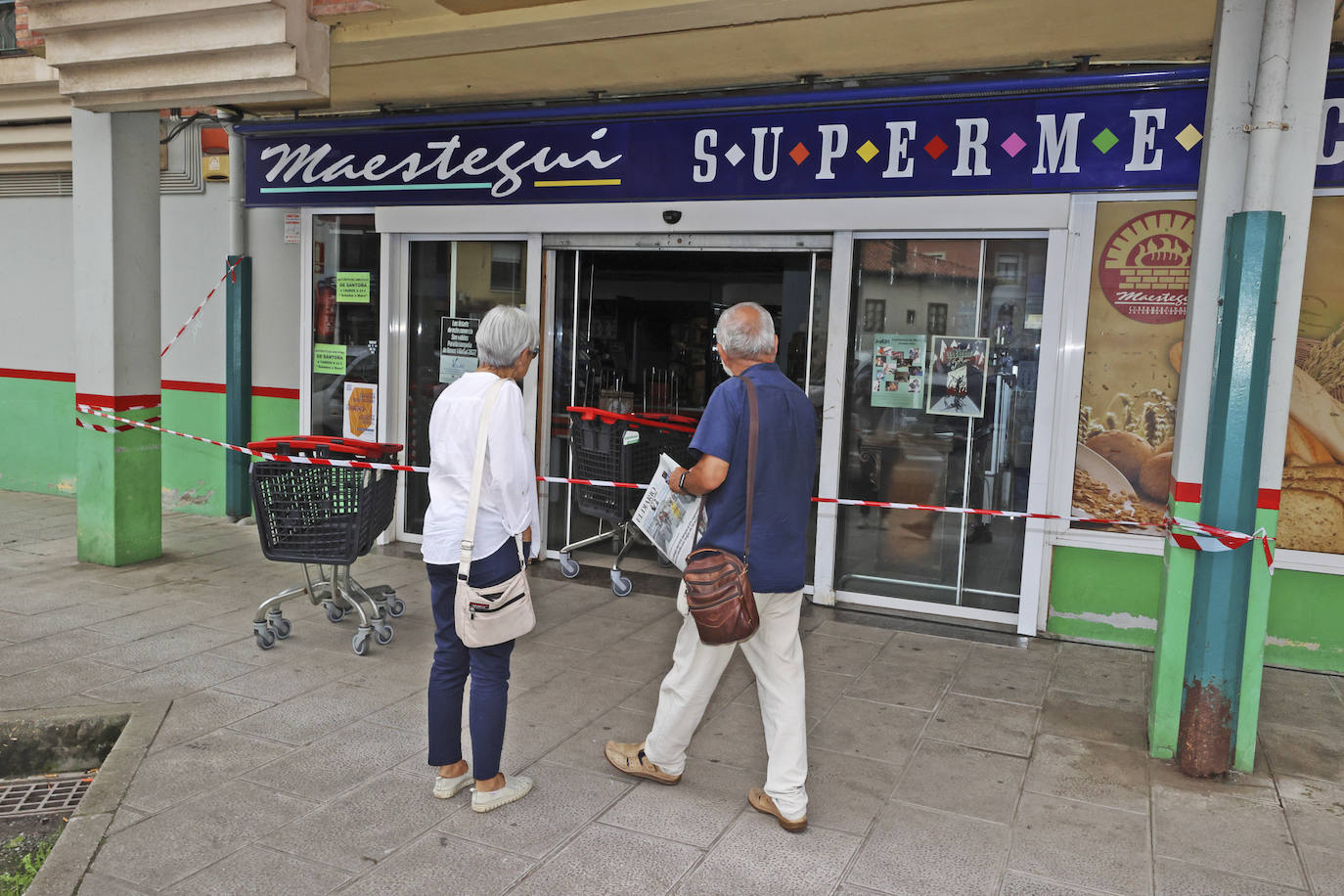 Dos personas miran el interior del supermercado afectado por las llamas detrás del precinto establecido.