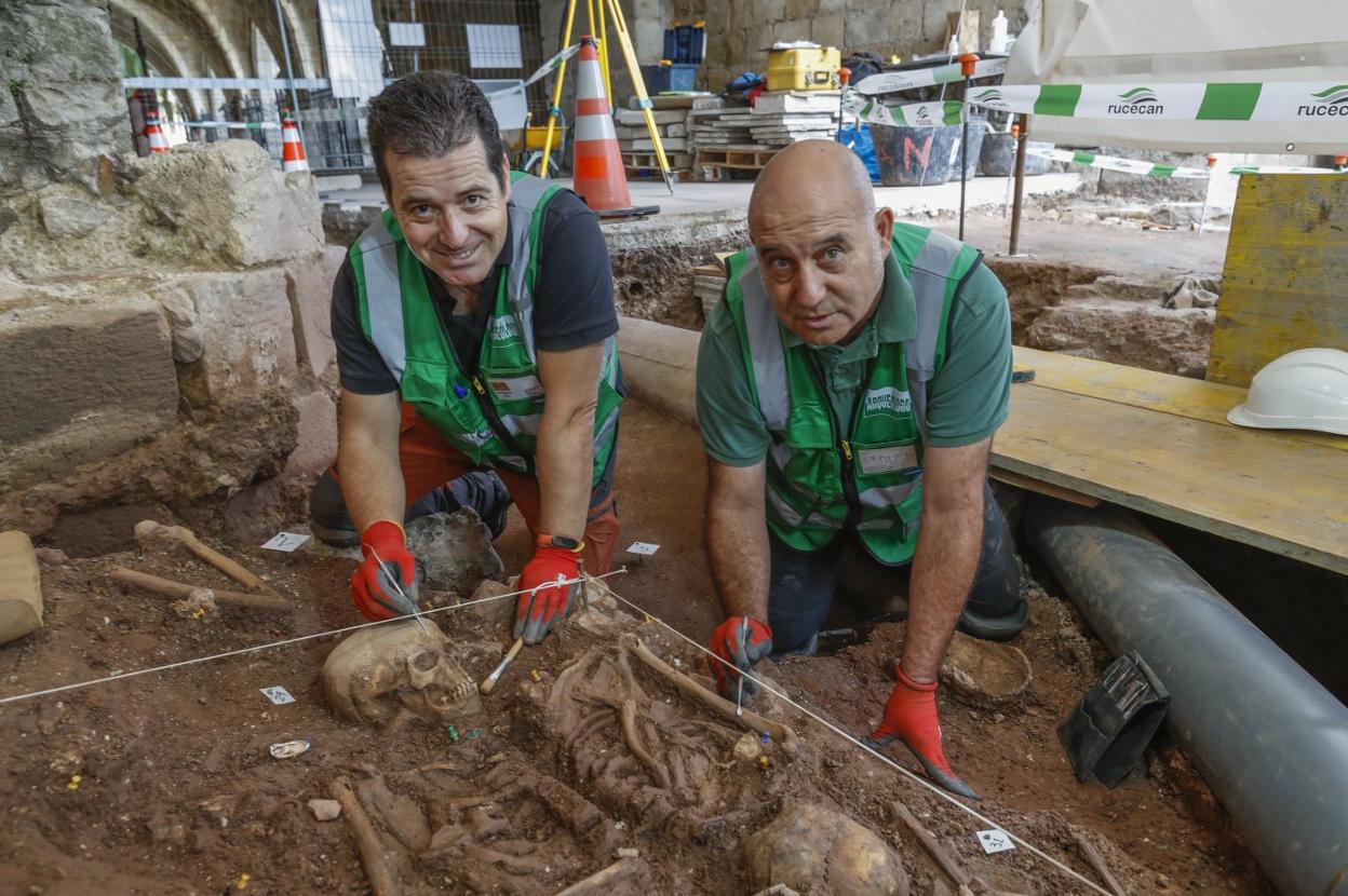 Los arqueólogos Lino Mantecón y Javier Marcos, junto a uno de los cuerpos localizados, con una moneda al cuello.