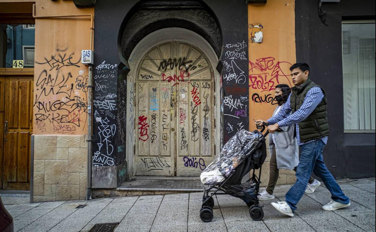 Una pareja pasea ante un portal lleno de pintadas.