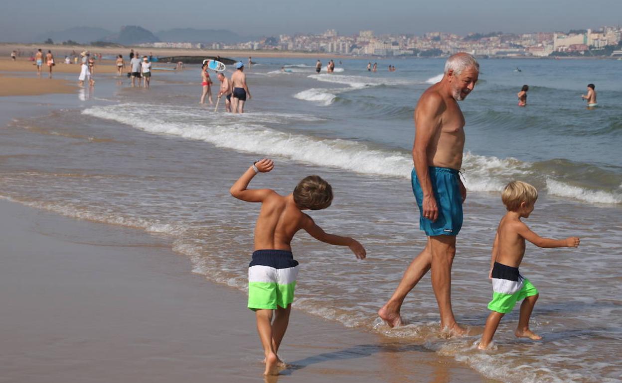 Dos niños juegan junto a su abuelo mientras entran a darse un chapuzón en la playa de Somo 