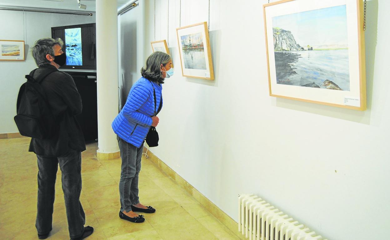 Dos visitantes contemplan la obra de Pomés en la Casa de Cultura de Santoña. 