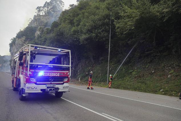 Los bomberos atacan las llamas en la ladera, encima de la carretera N-634.