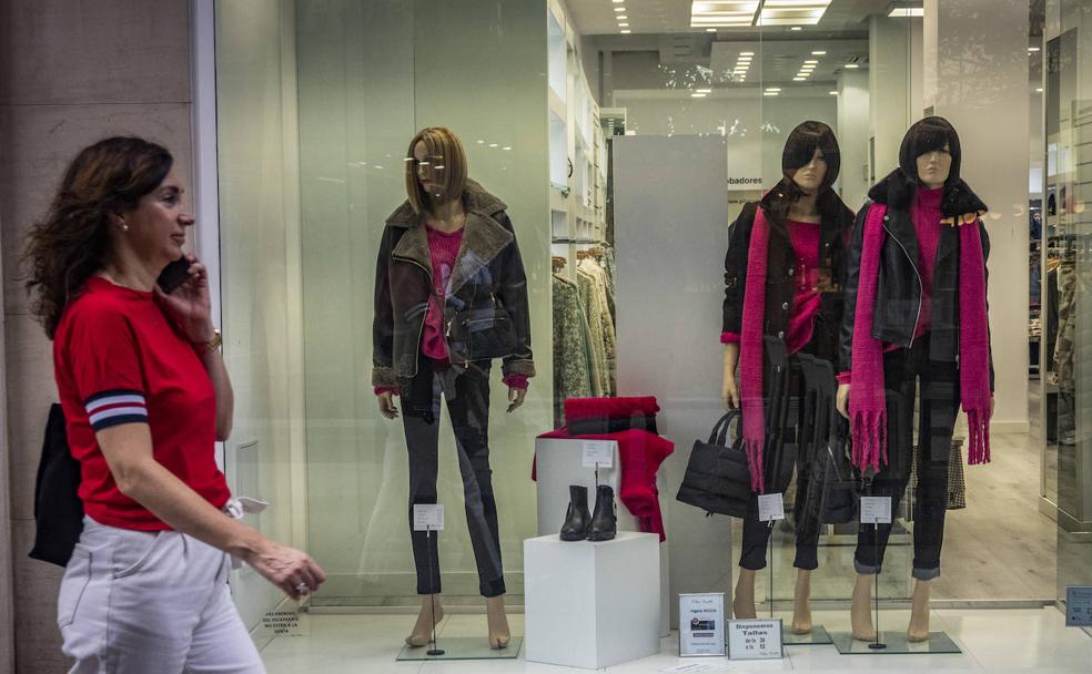 Una mujer, en manga corta, paseando ayer por Santander frente a un escaparate con ropa de abrigo. 