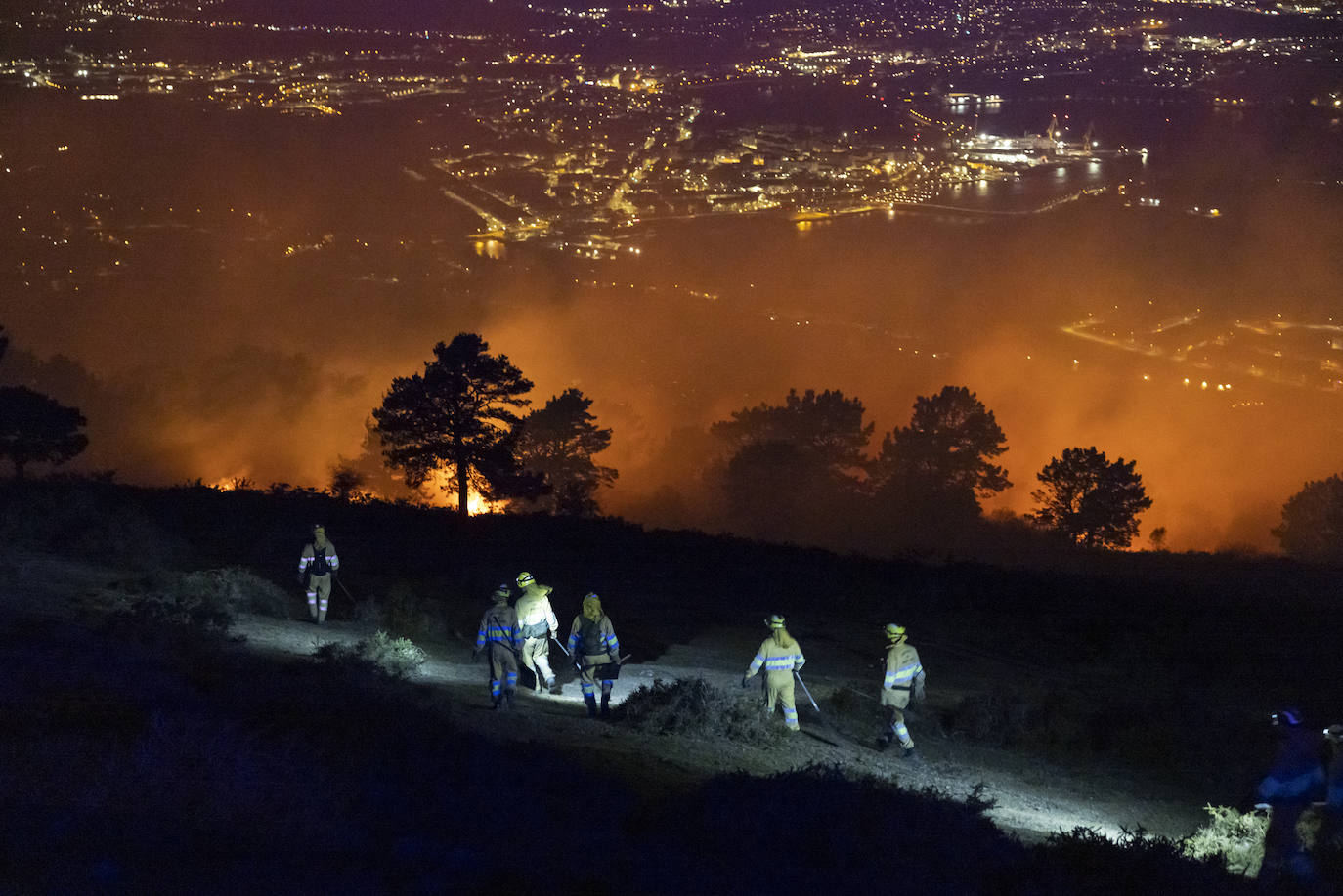 Seis agentes del medio natural se dirigen hacia uno de los focos activos en el macizo. Santander, de noche, al fondo.