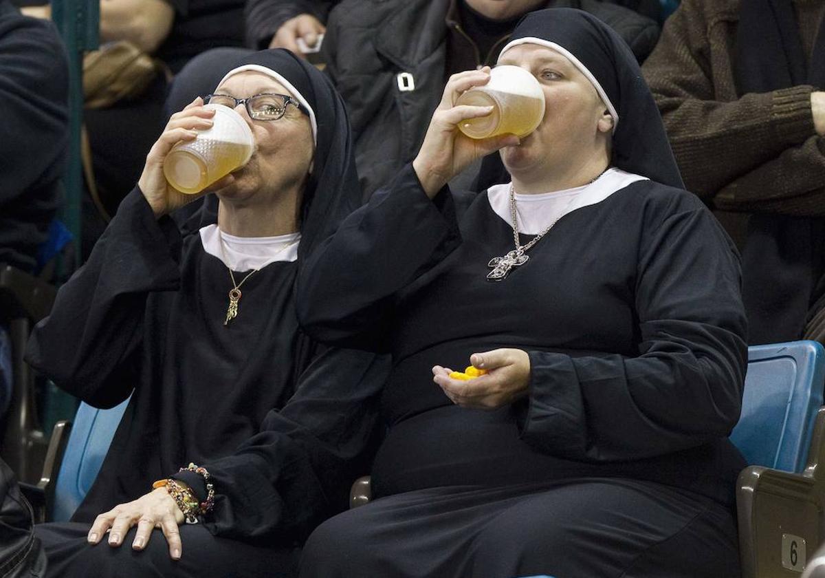 Dos mujeres disfrazadas de monjas beben cerveza en una grada