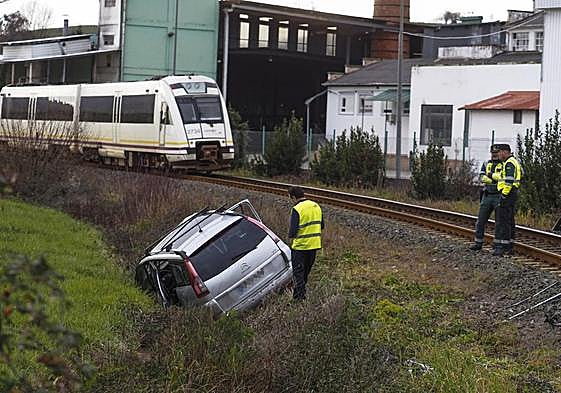 Agentes de la Guardia Civil inspeccionan el turismo siniestrado, que quedó recostado sobre la cuneta izquierda, con el tren detenido al fondo.