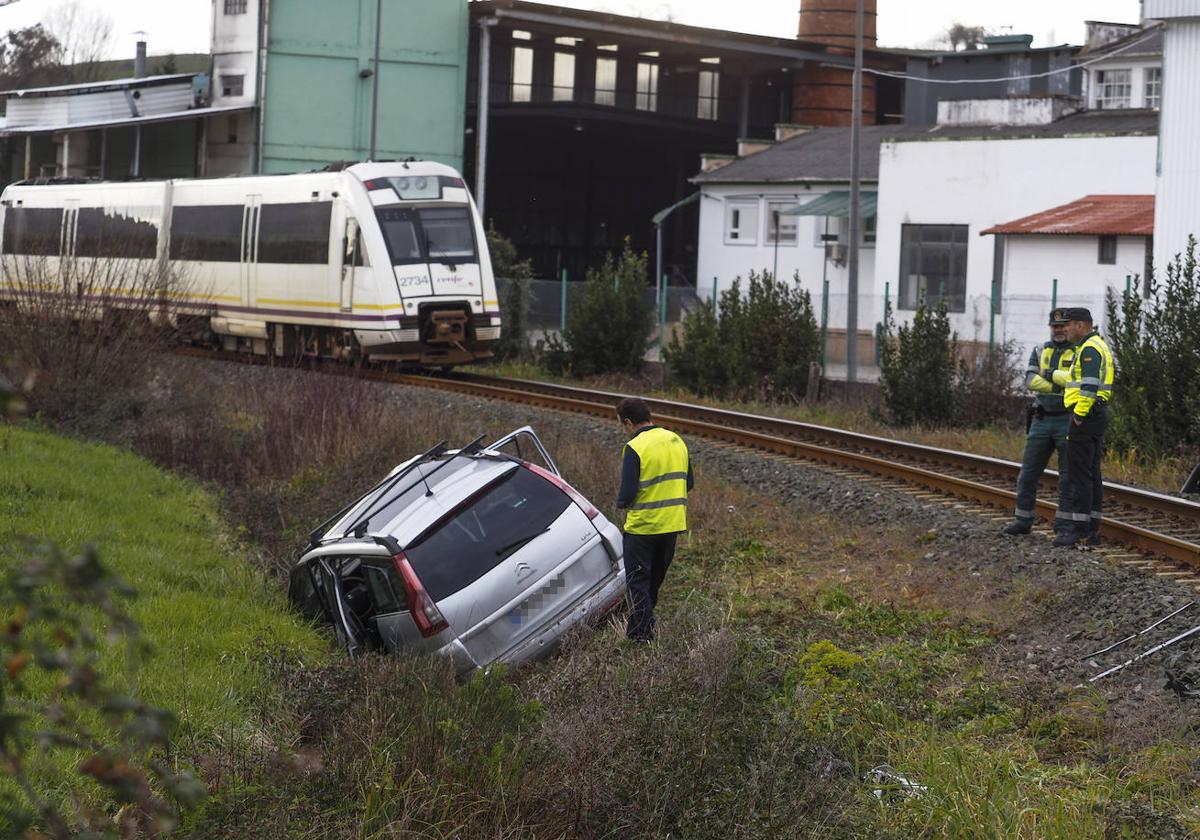 Agentes de la Guardia Civil inspeccionan el turismo siniestrado, que quedó recostado sobre la cuneta izquierda, con el tren detenido al fondo.