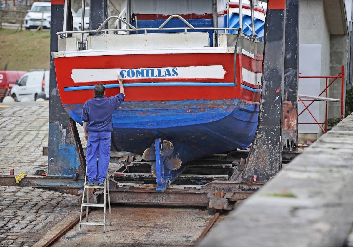 Un pescador pinta su barco en el muelle de Comillas.