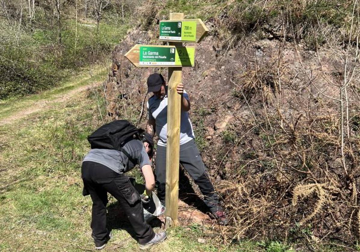 Dos operarios colocan uno de los paneles informativos de las rutas.