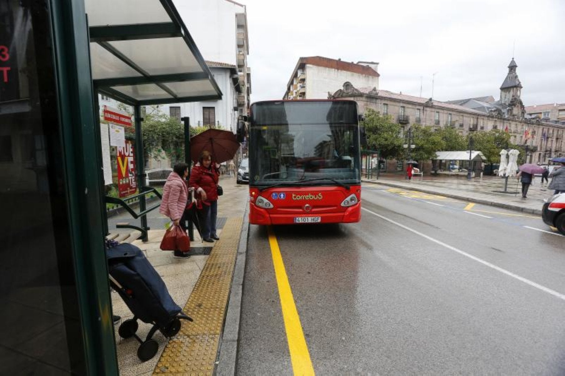 Usuarios del Torrebús aguardan a la llegada de un autocar, en la calle Julián Ceballos de Torrelavega.