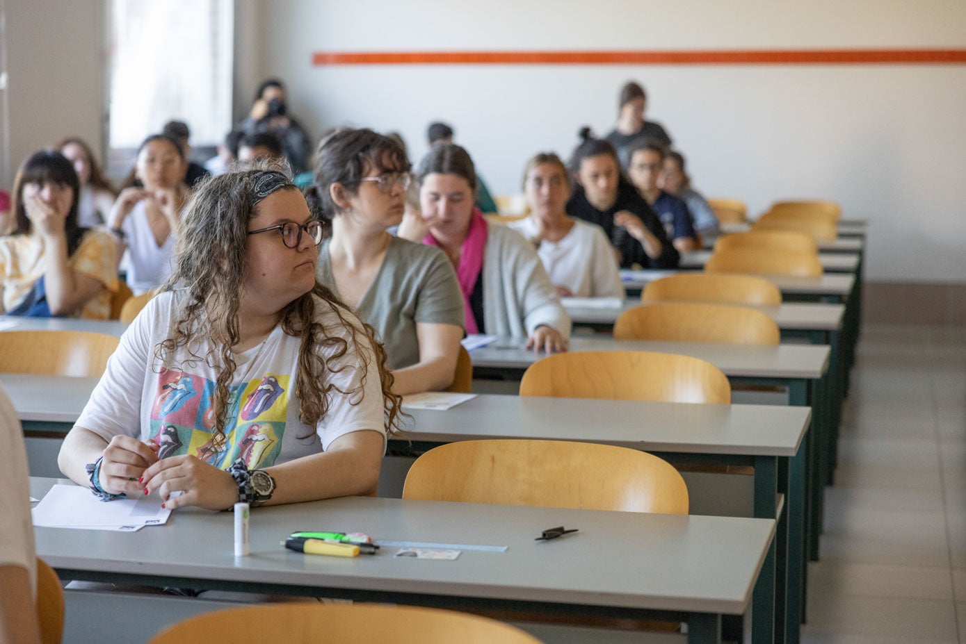 Los estudiantes antienden a las explicaciones con el material sobre la mesa y la documentación a la vista en las mesas, justo antes del reparto de exámenes.