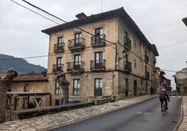 Un ciclista circula por delante de la Casa del Rivero en su vertiente a la carretera general, con la antigua lonja adosada a su cara trasera.