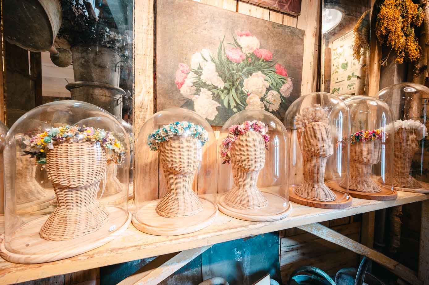 Diademas de flores secas sobre bustos de mimbre, cubiertos con urnas de cristal. 