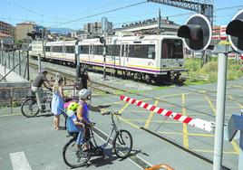 Peatones y ciclistas, esperan a que cruce un tren en el paso a nivel de Pablo Garnica, en Torrelavega.