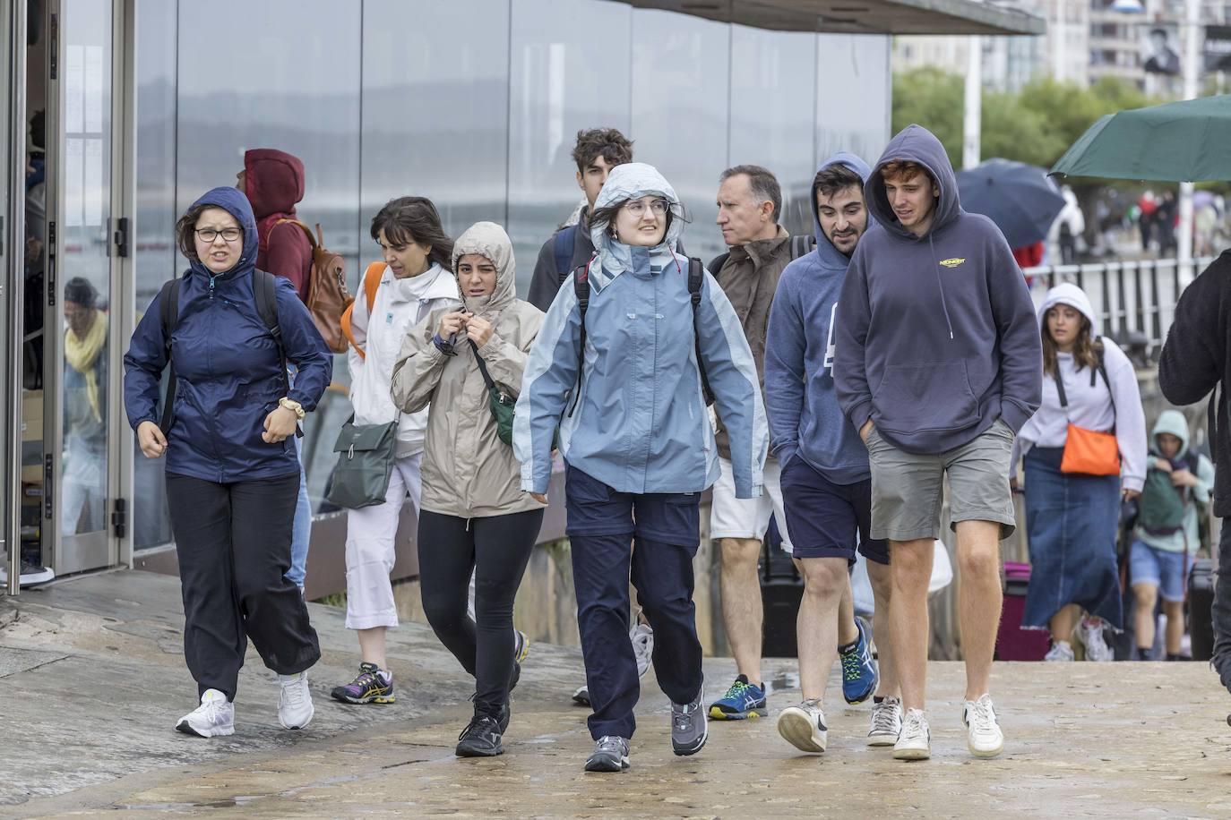 Un grupo de turistas se protege de la lluvia a su llegada a Santander.