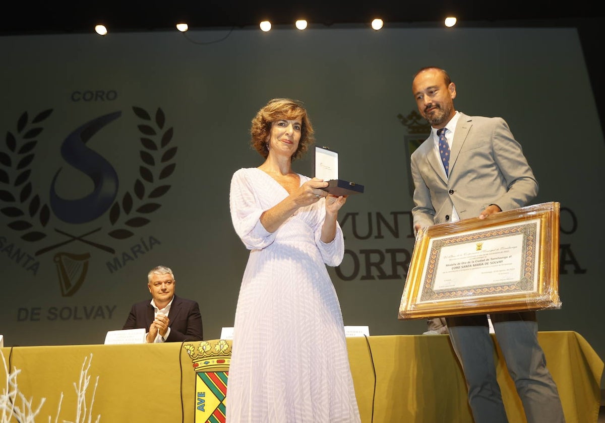 La presidenta de la entidad coral, Sonsoles Pérez, recibe la medalla de manos del alcalde, Javier López Estrada, este jueves, en el Teatro Concha Espina de Torrelavega.