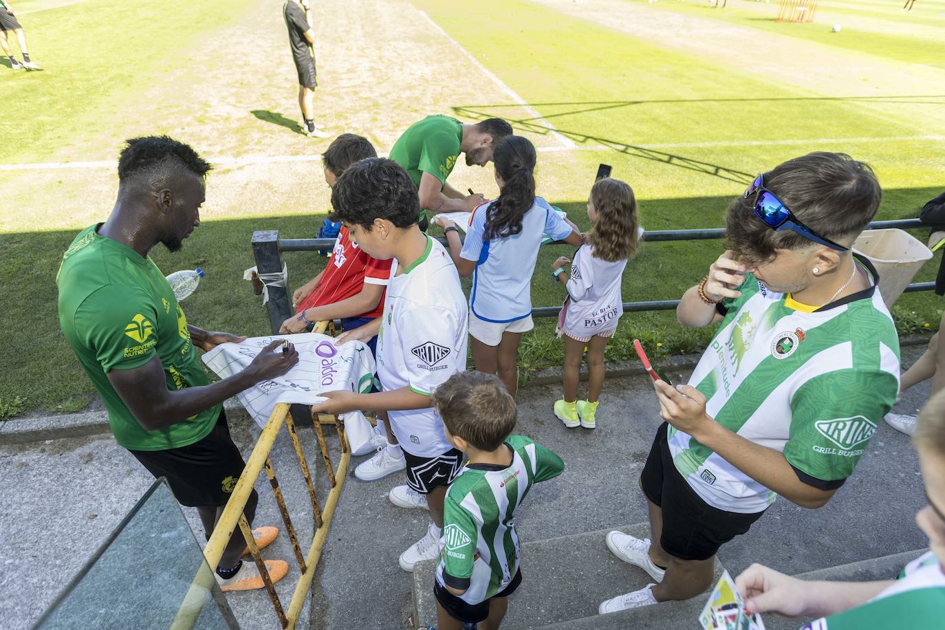 Lago Junior, en primer término, firma una camiseta, con Matheus Aiás en segundo plano haciendo lo mismo.