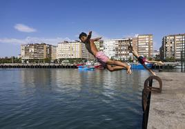 Dos jóvenes se lanzan al agua, este miércoles, desde uno de los muelles del Barrio Pesquero en Santander.