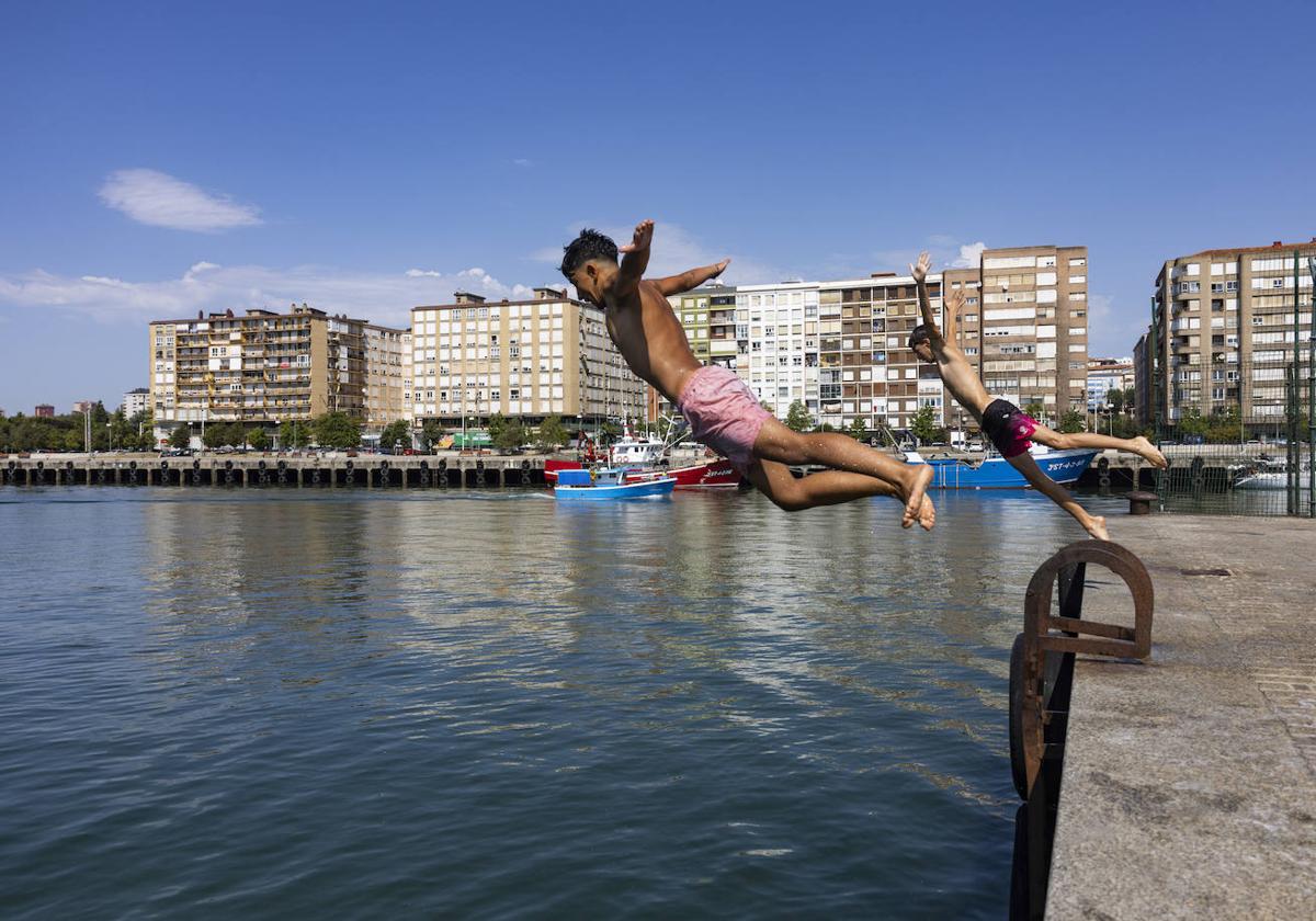 Dos jóvenes se lanzan al agua, este miércoles, desde uno de los muelles del Barrio Pesquero en Santander.