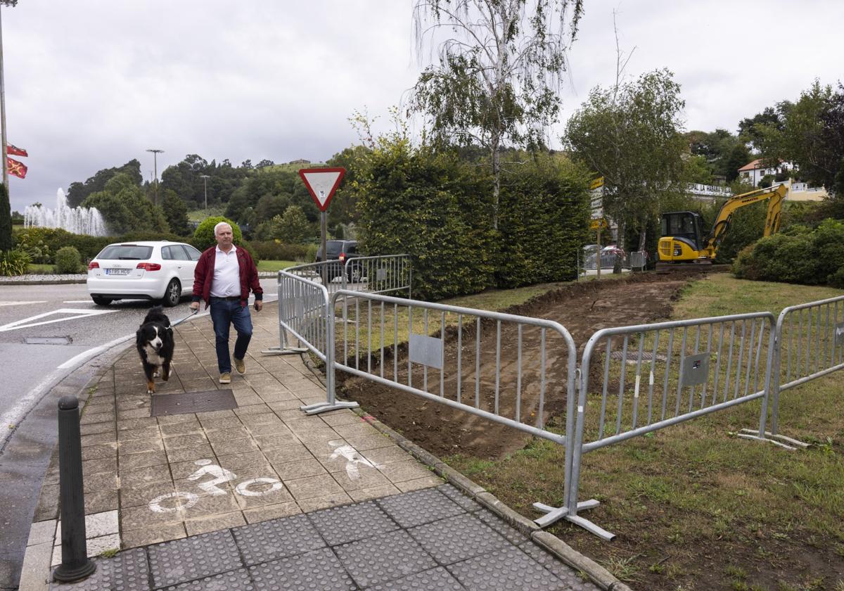 Un hombre pasea con su perro junto a la glorieta de entrada a la ciudad y la obra recién iniciada en La Inmobiliaria.