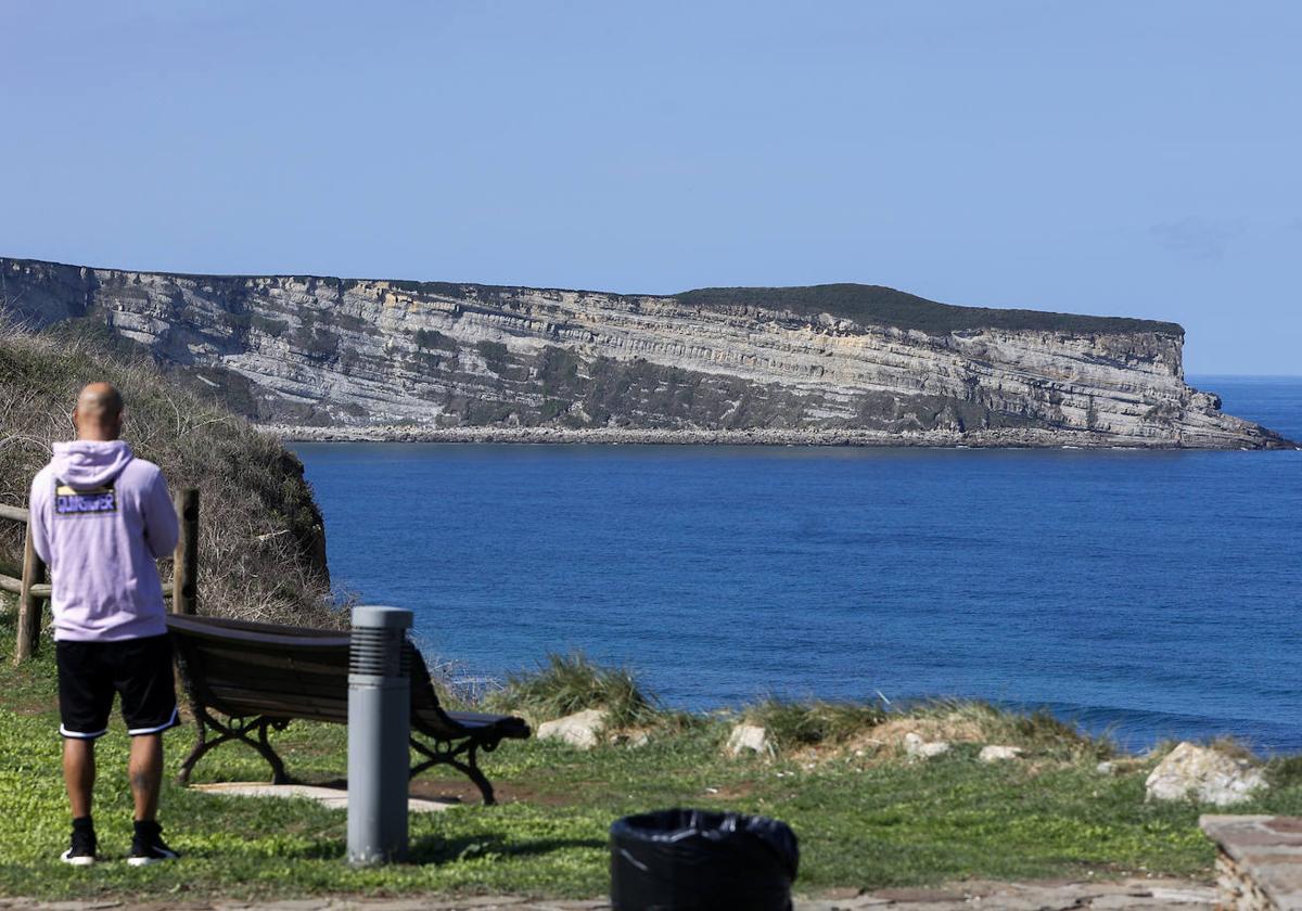 Una persona contempla desde Suances la zona de Punta Ballota, el saliente en el mar que aparece al fondo de la fotografía.