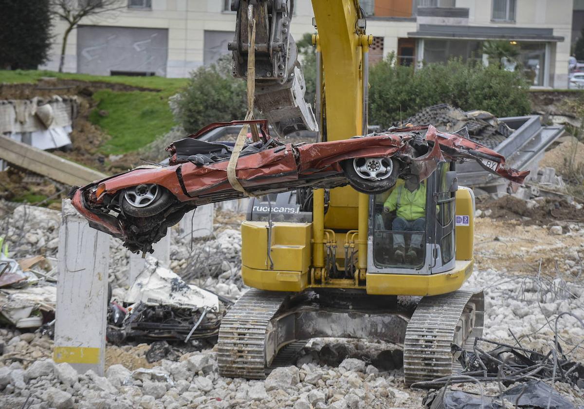 La maquinaria saca coches aplastados de los garajes de Nueva Montaña tras el derrumbe.