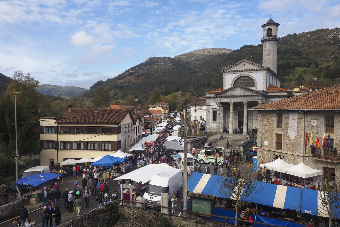 La gente camina por la calle principal de la localidad junto a la iglesia de San Pelayo.