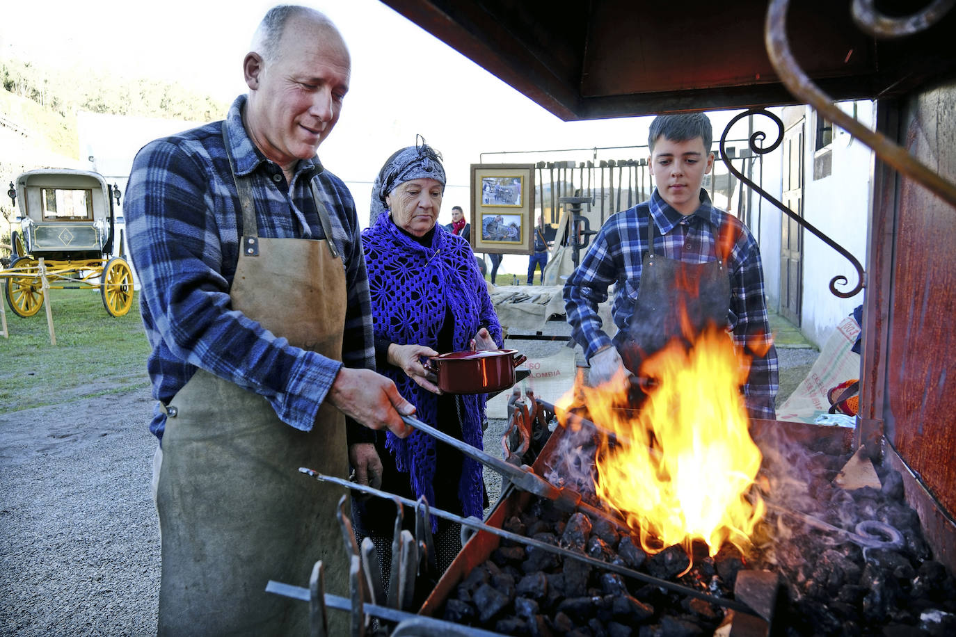 Dos adultos y un joven preparan los alimentos a la brasa. 