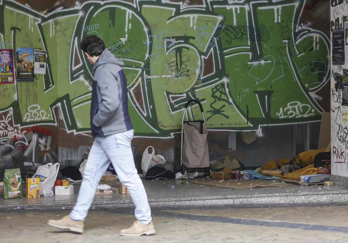 Un peatón cruza frente a una persona sin hogar y su mascota, este invierno, en Torrelavega.