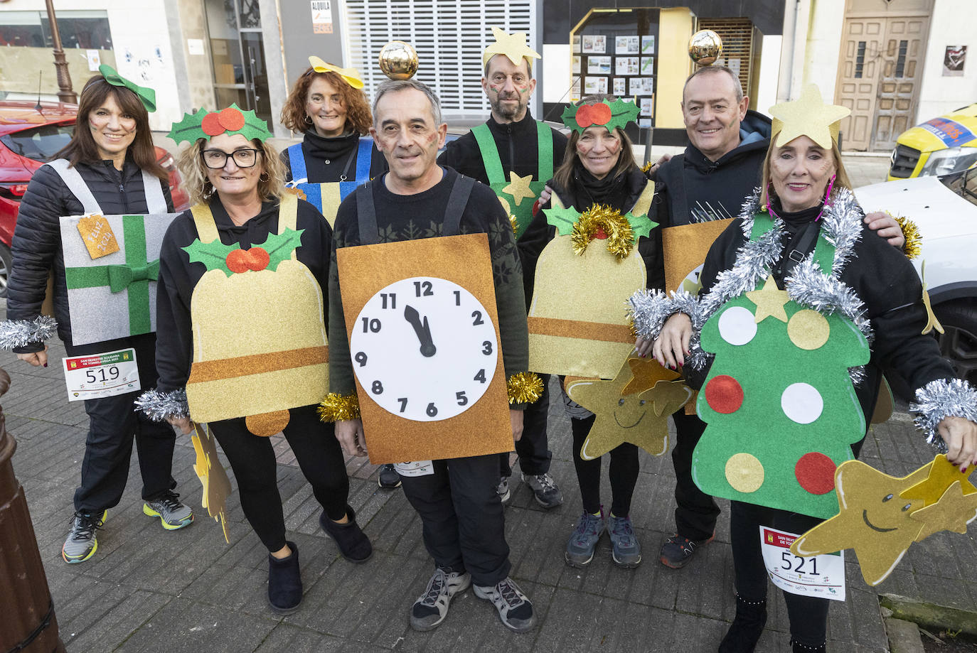 Un grupo de atletas, disfrazado de regalos, árbol de navidad, campanas y reloj que marca casi las doce.