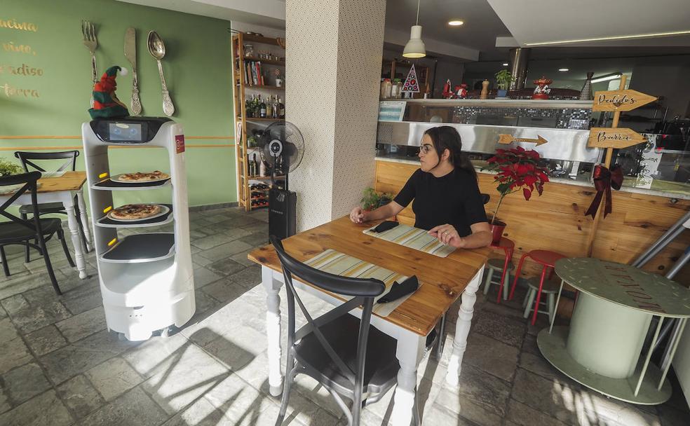 Maru García, en la mesa, espera la llegada de las pizzas que le trae el robot. 