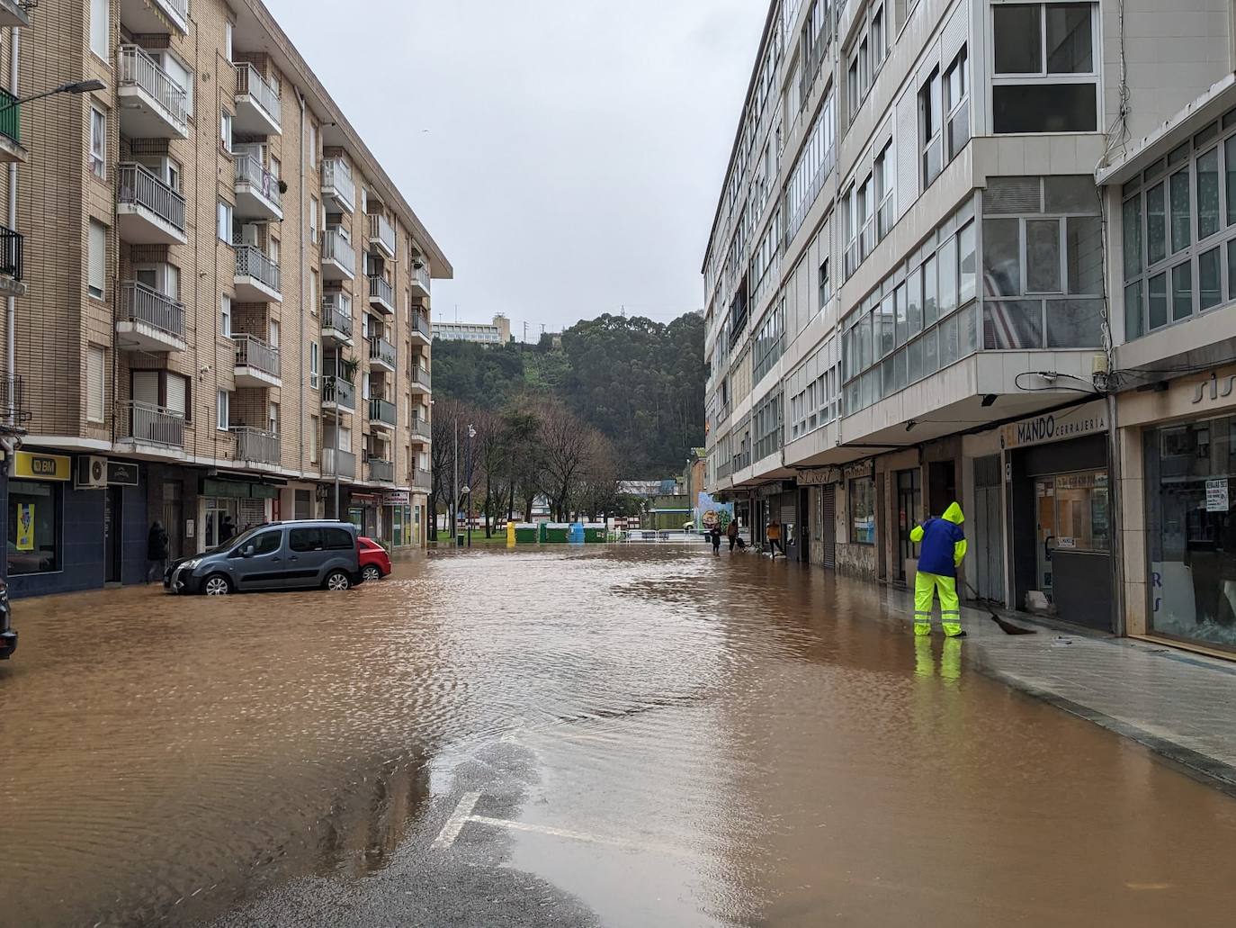 Un operario barre las aceras mientras el agua no deja de subir en Martínez Balaguer (Laredo).