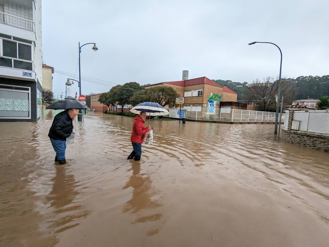 Dos vecinos cruzando en la confluencia de Marqués de Valdecilla con la Avenida de España, en Laredo, con el agua más arriba de las rodillas.