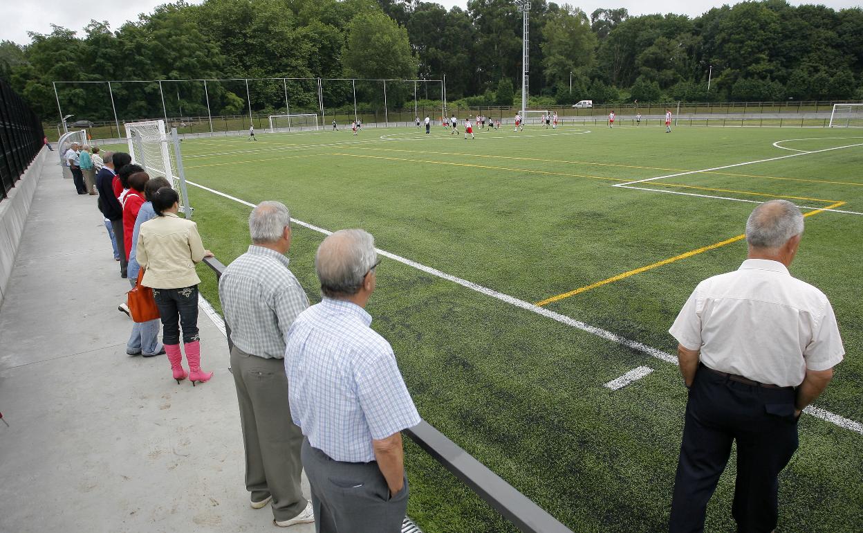 Un grupo de aficionados presencia un partido en el campo de fútbol de hierba artificial. 