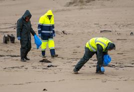 Los operarios de la empresa pública Tragsa retiran los pélets encontrados en la playa de Valdearenas, en Liencres.