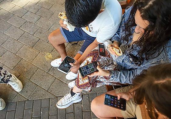 Tres jóvenes utilizan su teléfono móvil