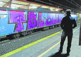 Un pasajero ve desde el andén cómo llega un tren lleno de grafitis.