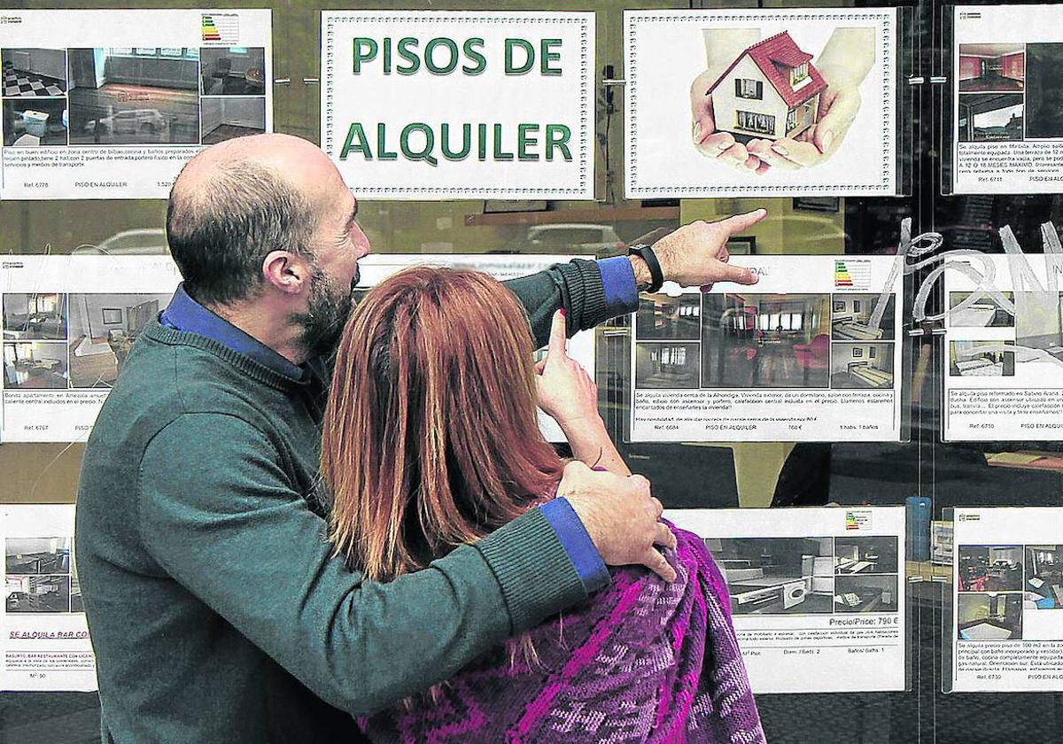 Una pareja obseva los anuncios de pisos de alquiler en una agencia inmobiliaria.