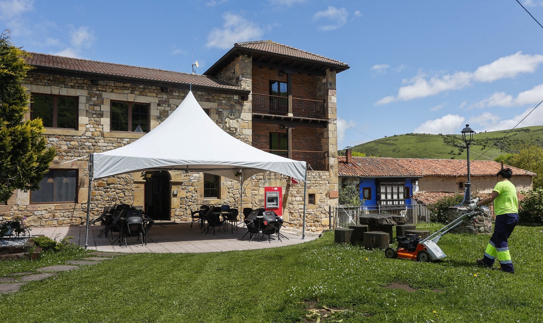 Tania Saiz, una de las nueve personas que trabajan como operarios municipales, pasa la máquina de segar frente al único bar de San Miguel de Aguayo.