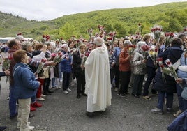 El párroco rodeado de fieles con rosas en la procesión.