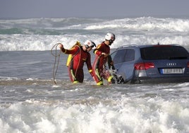 Dos rescatadores del 112 trabajan en el amarre del coche a un tractor que se empleó para sacarlo del mar.