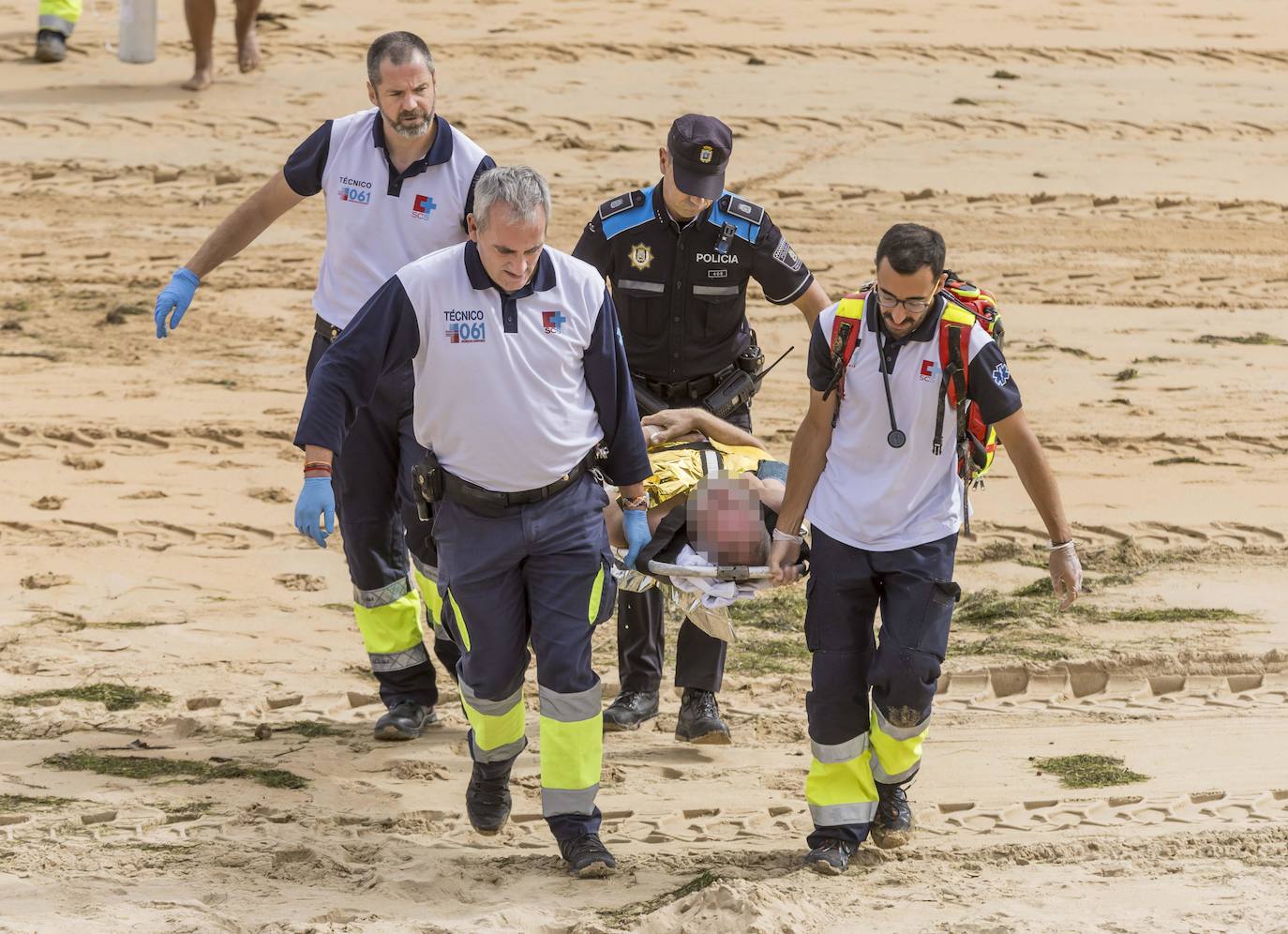 Profesionales del equipo del 061 y un policía trasladan a un paciente indispuesto en la playa.